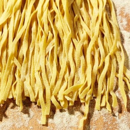 Auf einem Holzbrett liegt ein Stapel Taglierini | Pasta
