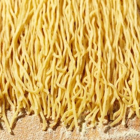 Auf einem Holzbrett liegt ein Stapel Tonnarelli | Pasta