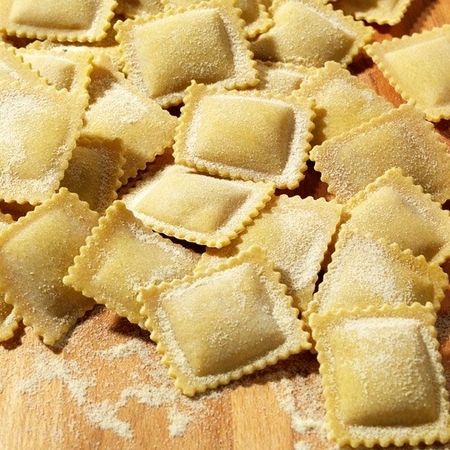Nahaufnahme und Zubereitung von Ravioli (Sorte: Steinpilz) auf einem Holzbrett