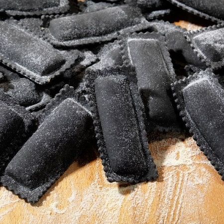 Nahaufnahme und Zubereitung von Ravioloni (Sorte: Schwarz) auf einem Holzbrett