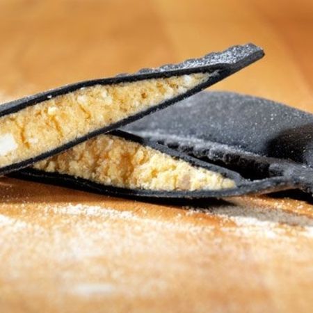 Nahaufnahme und Zubereitung von Ravioloni (Sorte: Hummer, Schwarz) auf einem Holzbrett