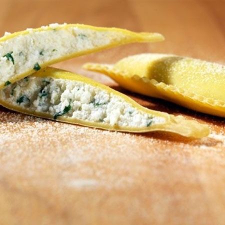 Nahaufnahme und Zubereitung von Ravioloni (Sorte: Rucola) auf einem Holzbrett