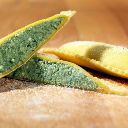 Nahaufnahme und Zubereitung von Ravioloni (Sorte: Spinat) auf einem Holzbrett