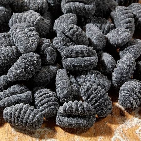 Schwarze Gnocchi präsentiert auf einem Holzbrett mit Mehl