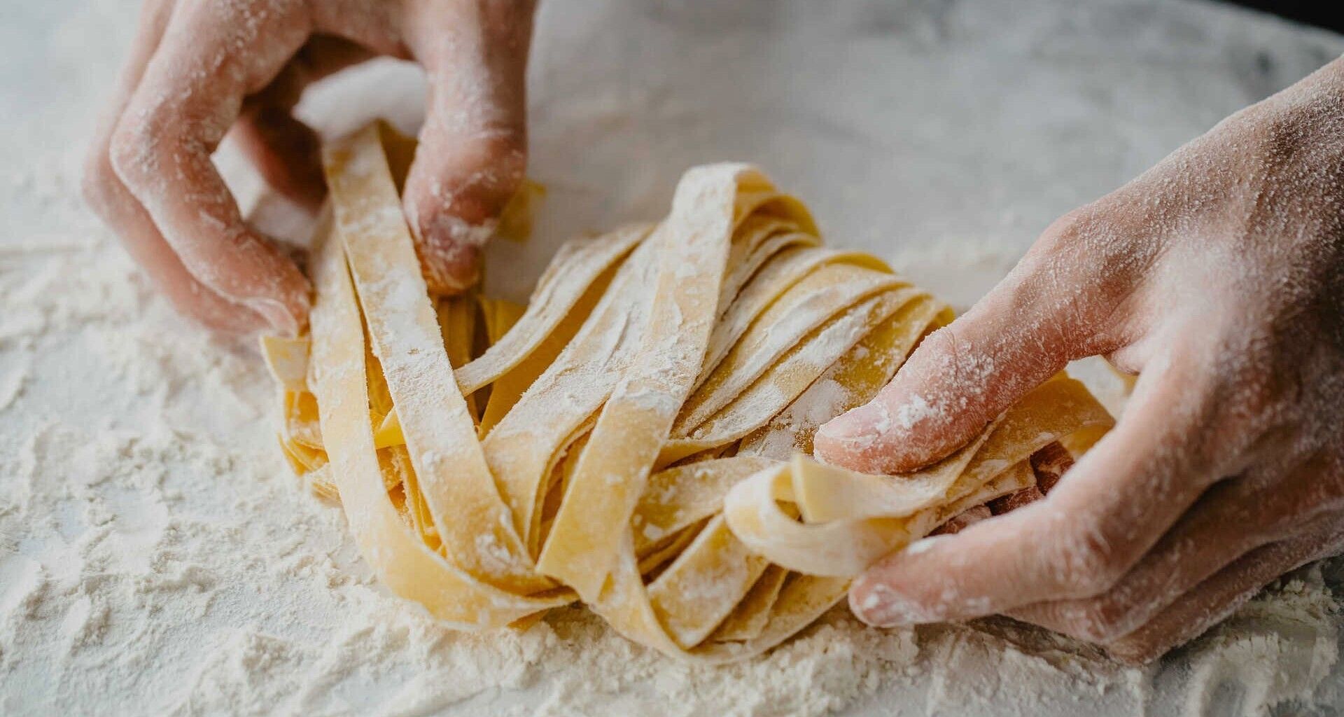 Eine Person hält ein Stück Pasta auf einem Tisch